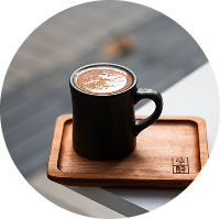 Café caliente con arte latte servido en taza negra sobre bandeja de madera